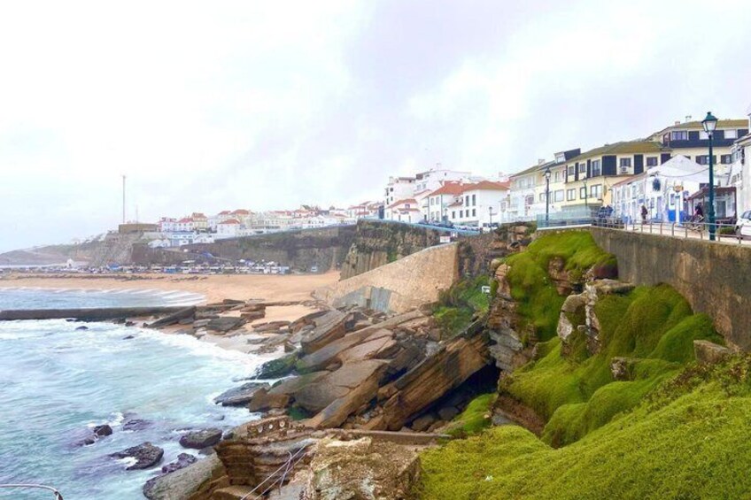 A coastal town with buildings along the cliff, waves crashing against the rocks, and a grassy embankment. 5