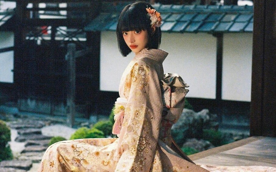 A person in traditional attire with floral patterns, standing in front of a building with a tiled roof. 2