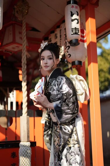 A person in traditional Japanese attire standing in front of a shrine with red pillars and white lanterns. 5