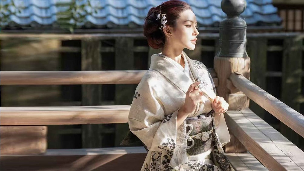 A person in traditional attire standing on a wooden bridge with a railing. 1