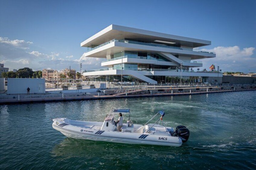 A modern building with a flat roof and a boat on the water in front. 1