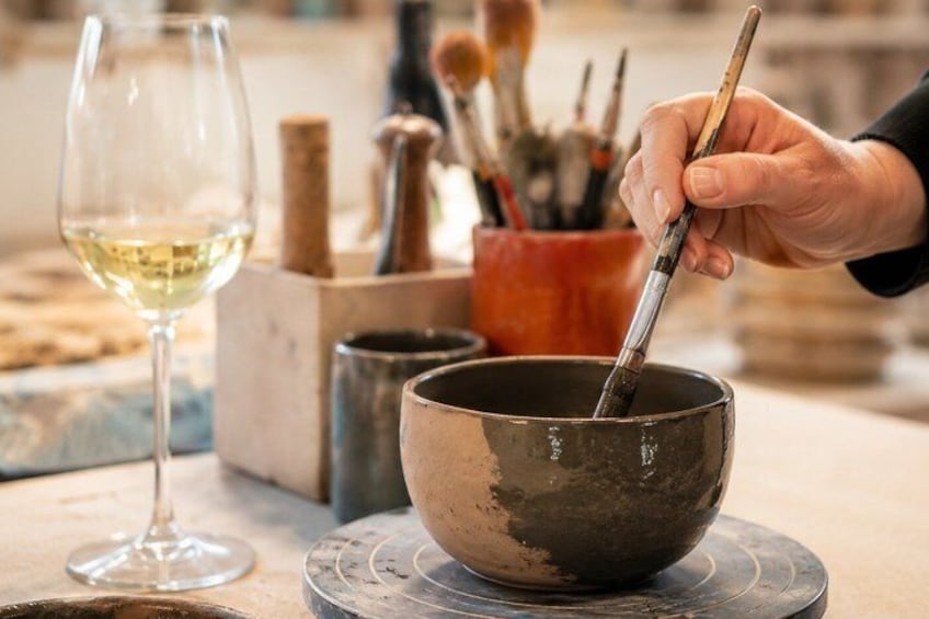 A person stirring a bowl with a brush, a wine glass, and a container of brushes on a table. 1