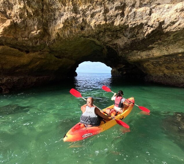 Two people kayaking in clear water under a rocky cave. 5