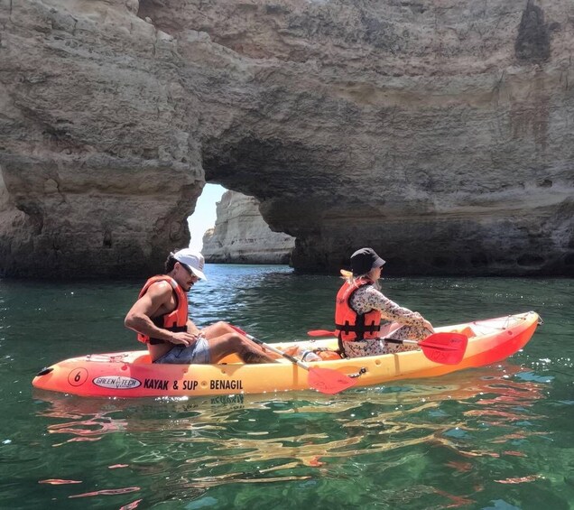 Two people kayaking in a clear cove with a rocky backdrop. 4