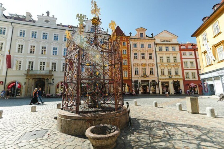 A historic square with cobblestone pavement, a central metal sculpture, and colorful buildings. 4