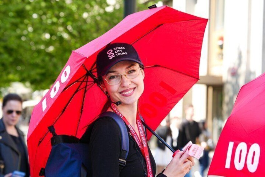 A person holding a red umbrella with '100' on it, wearing a black cap, and carrying a blue backpack. 1