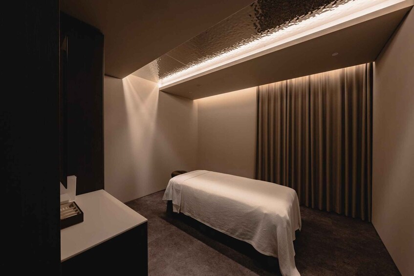 A dimly lit room with a single bed, a small table, and a curtain. 3