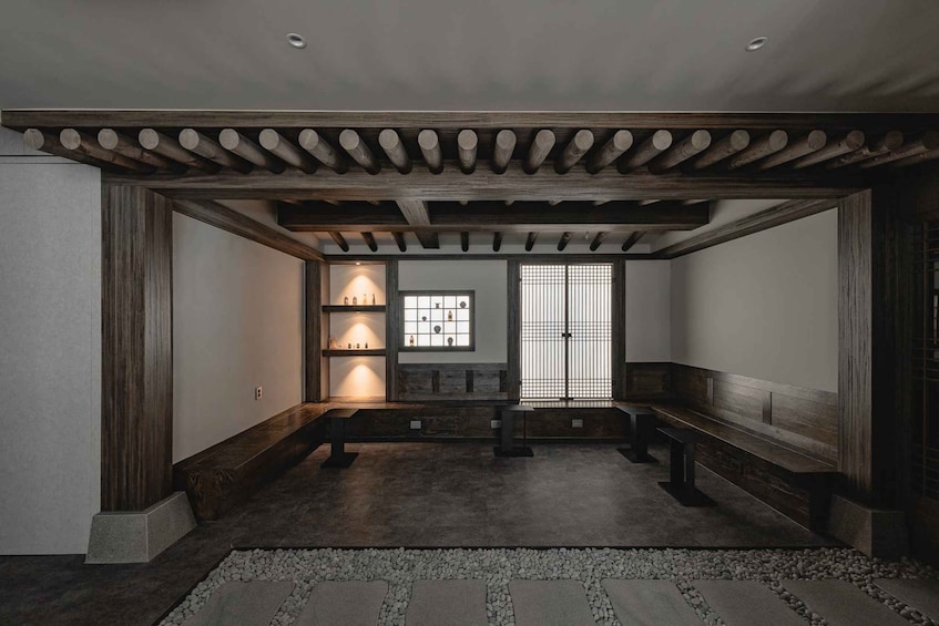 A traditional interior with wooden beams, benches, a tiled floor, and a window with a grid pattern. 1