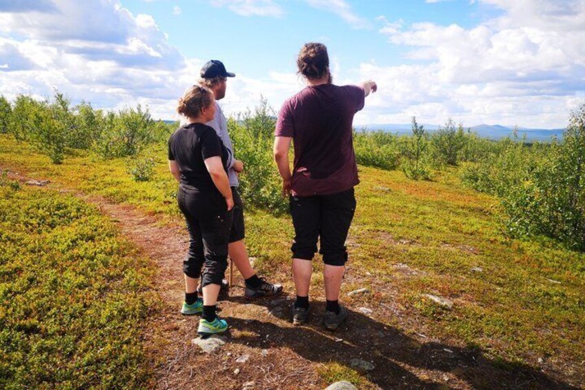 Three people standing on a grassy path with a mountainous landscape in the background. 4