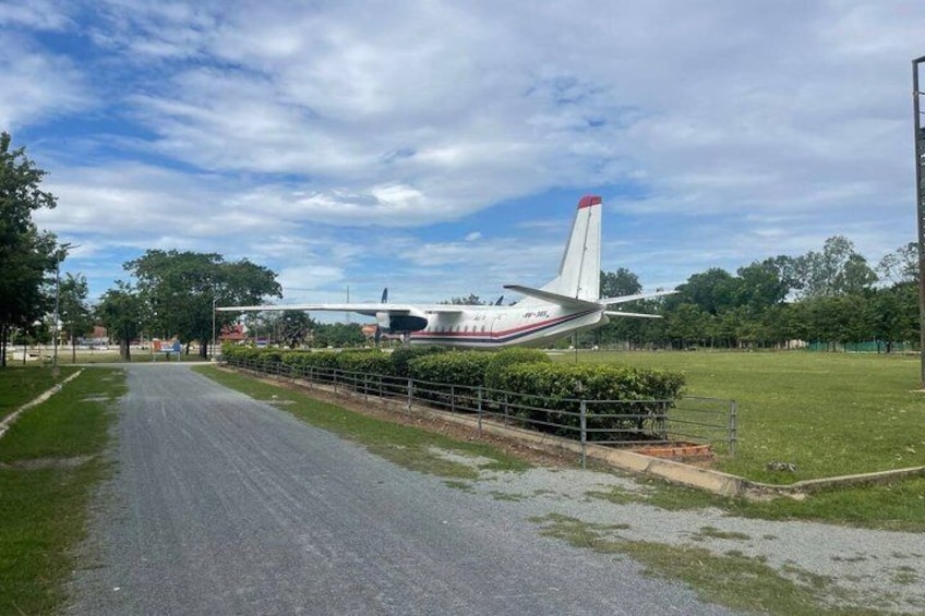 A small aircraft parked on a grassy field with a paved road in the foreground. 5