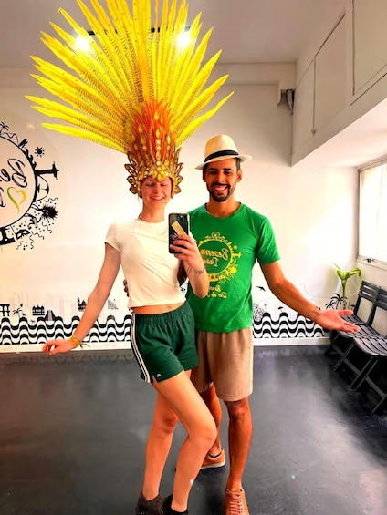 Two people in a room with a mural of a cityscape and a large yellow decorative headpiece. 1