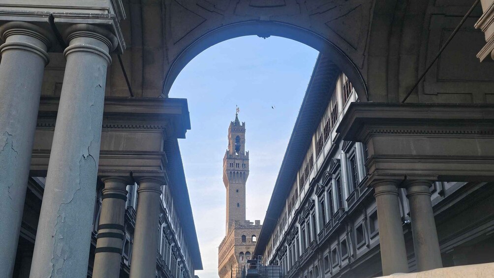 An archway framing a tall tower with a clock, surrounded by classical architecture. 1