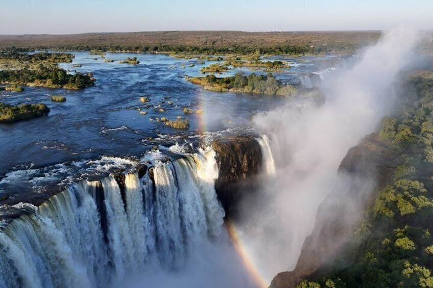 A waterfall with a rainbow, surrounded by greenery and a river. 1