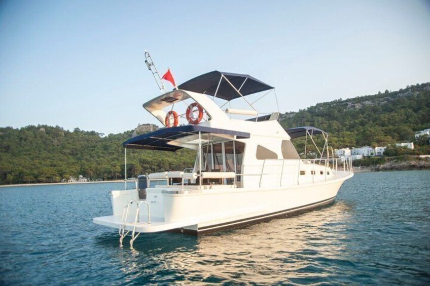 A white boat with a canopy and lifebuoys on calm water, surrounded by a hilly landscape. 4