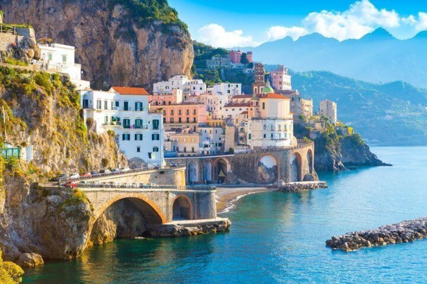 A coastal town with a stone bridge, colorful buildings, and a clear blue sea. 2