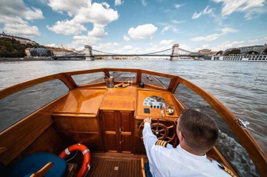 A boat with a wooden interior, a steering wheel, and a person in a white shirt at the helm. 1
