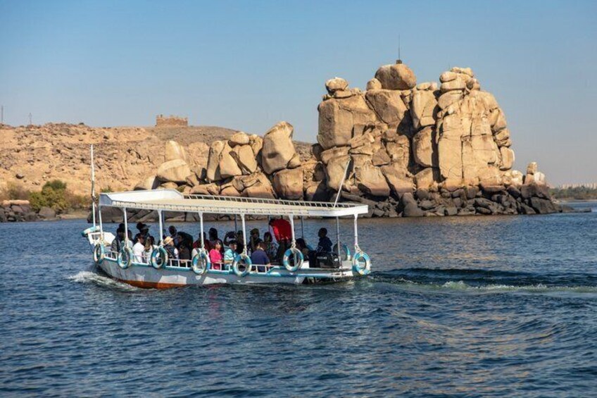 A boat with passengers on a calm river, with large rock formations in the background. 2