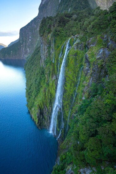 A waterfall cascading down a steep cliff into a deep blue body of water, surrounded by lush green vegetation. 4