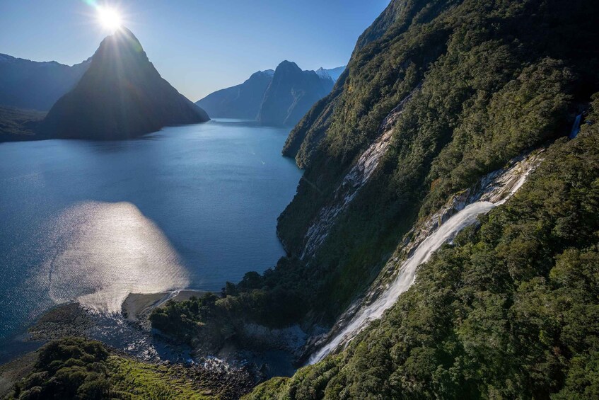 A mountainous landscape with a waterfall, a lake, and a sunlit peak. 1