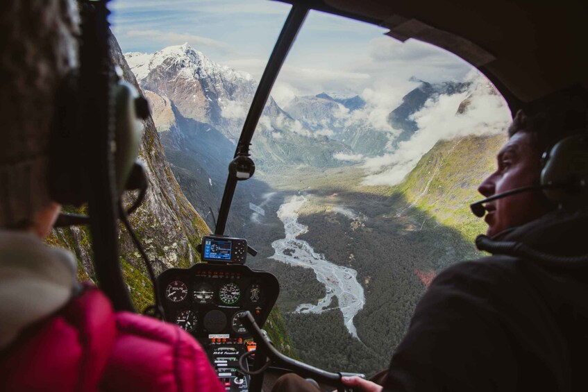 A helicopter cockpit with a view of a mountainous landscape, including a river and snow-capped peaks. 3