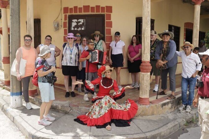 A group of people gathered outside a building with a person in a red and black traditional dress performing. 1