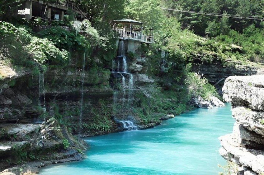 A turquoise river flowing through a rocky gorge with a waterfall and a viewing platform. 1