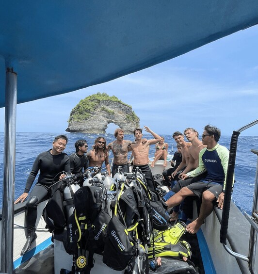 A group of people on a boat with scuba diving gear, a rocky island in the background, and clear blue water. 3
