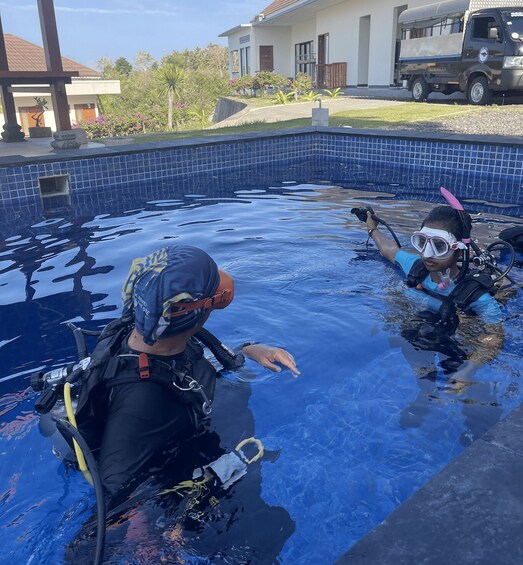 Two people in a swimming pool with scuba gear, a truck, and a house in the background. 5
