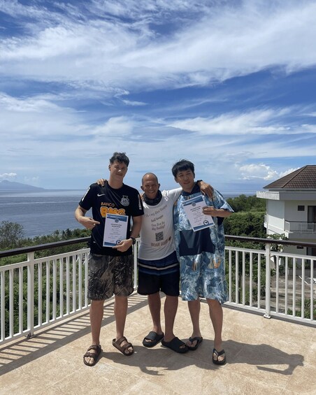 Three people on a balcony with certificates, overlooking a coastal landscape. 2