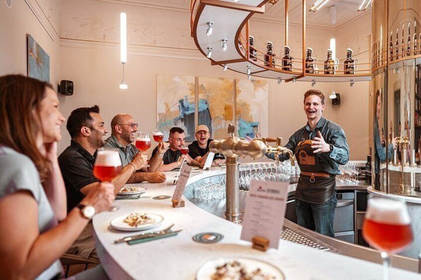 A group of people seated at a bar, holding glasses of red wine, with a bartender standing behind them. 5