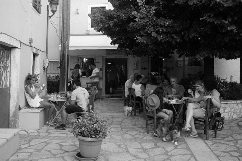 People sitting at tables outside a building, a dog, and a potted plant. 1