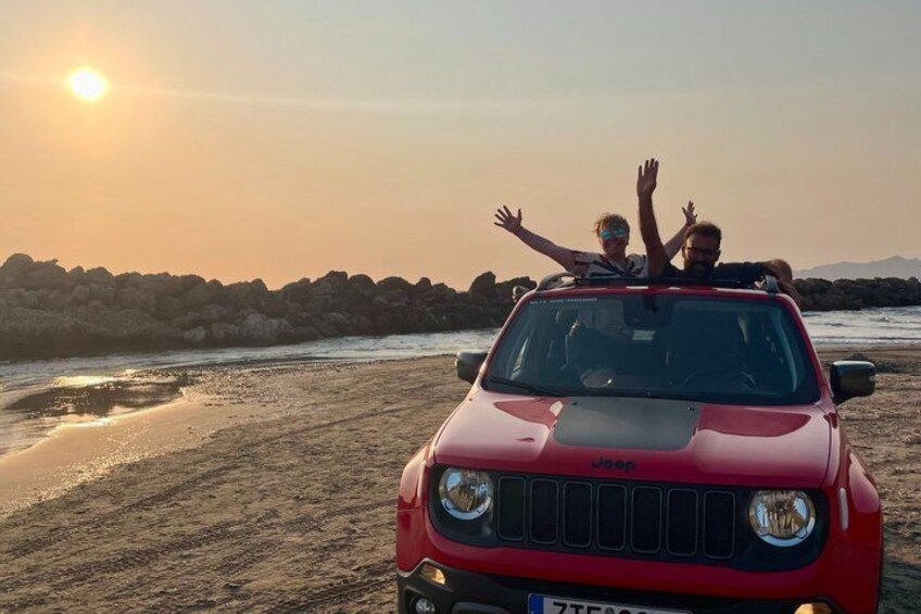 En röd Jeep står på en sandstrand med en solnedgång i bakgrunden. 1