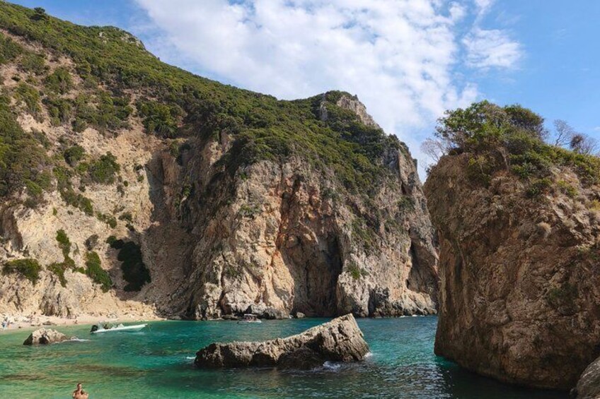 A coastal landscape with rocky cliffs, clear turquoise water, and a person swimming. 1