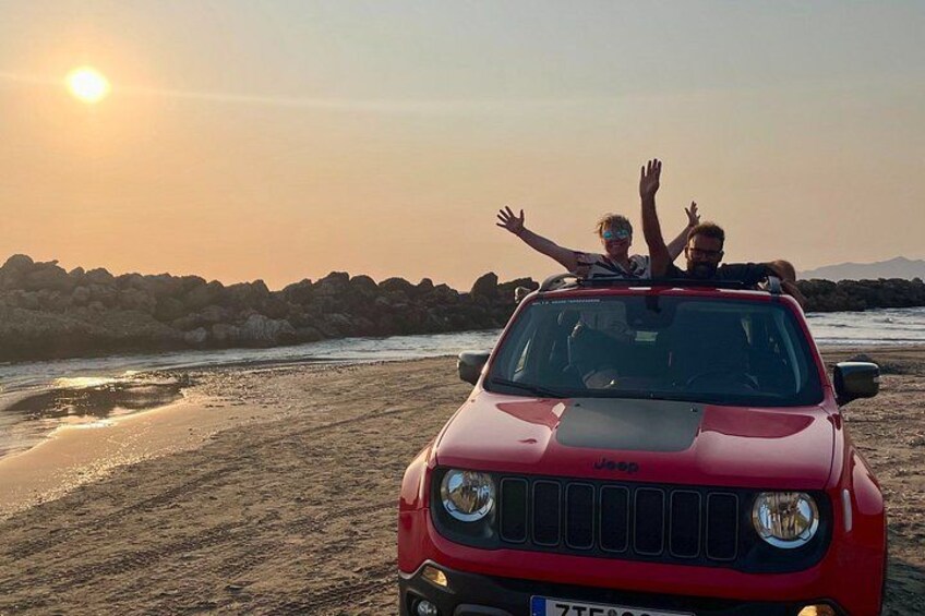 A red Jeep on a beach with two people raising their hands. 1