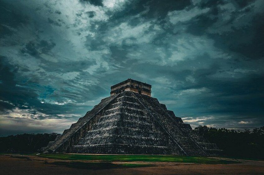 A large pyramid structure with a flat top, surrounded by a green field, under a cloudy sky. 5