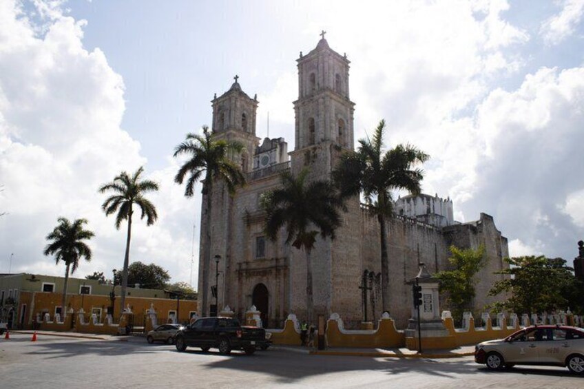 A historic cathedral with a bell tower, palm trees, and a yellow wall. 4