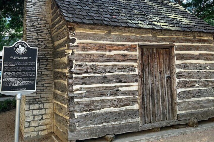 A log cabin with a weathered wooden door and a historical marker plaque. 4
