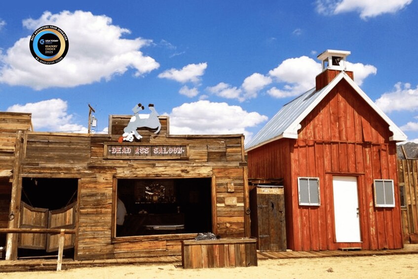 A rustic wooden building with a sign reading 'Dead Ass Saloon' and a red barn in the background. 1