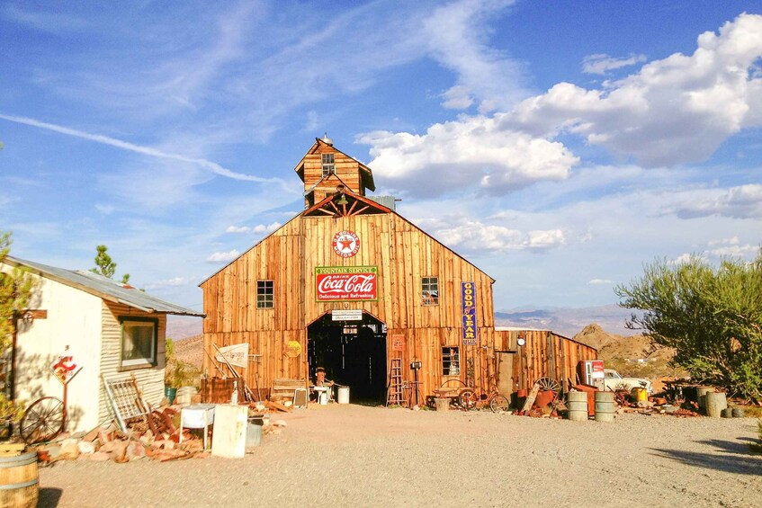 A wooden barn with a Coca-Cola sign, surrounded by desert vegetation and a clear sky. 5
