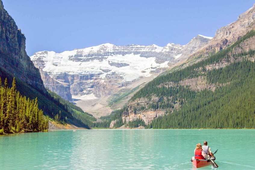 A canoe on a turquoise lake surrounded by forested mountains and snow-capped peaks. 5
