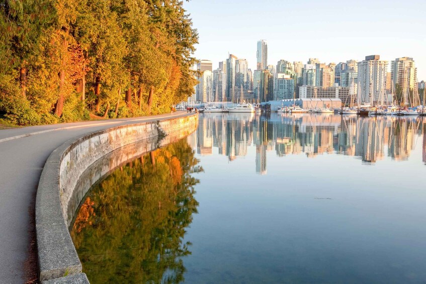 A waterfront with a city skyline reflected in calm water, surrounded by trees. 5