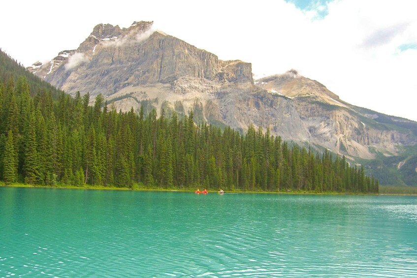 A calm lake with clear turquoise water, surrounded by dense green forest and a mountain range in the background. 4