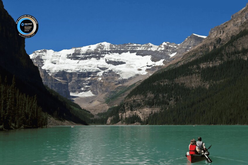 A person in a boat on a turquoise lake surrounded by mountains and snow-capped peaks. 1