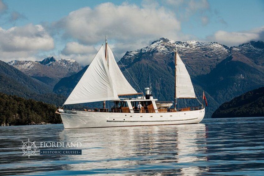 A sailboat on calm waters with a mountainous backdrop. 1