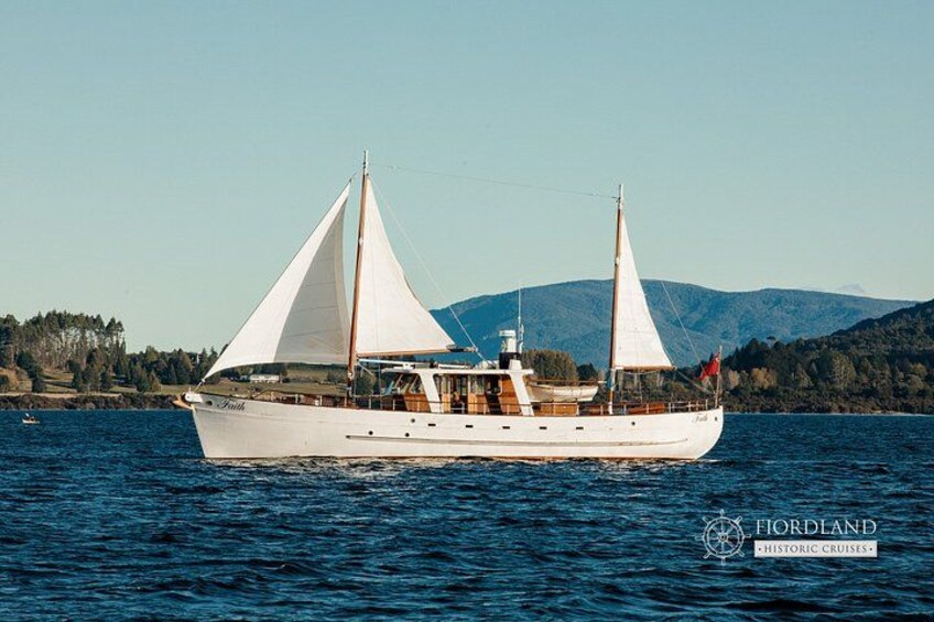 A white sailboat with two masts on a calm body of water, surrounded by a hilly landscape. 3