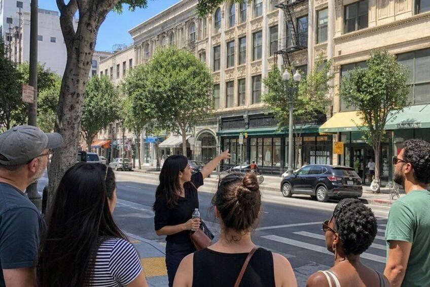 A group of people standing on a city street, looking towards a building across the road. 5