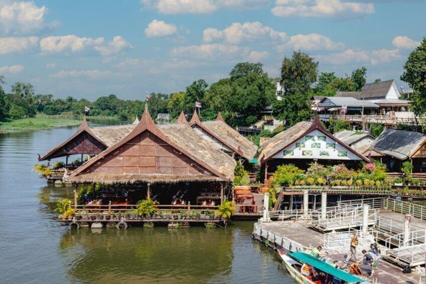 Floating houses with thatched roofs by a calm river, surrounded by greenery and a clear sky. 2