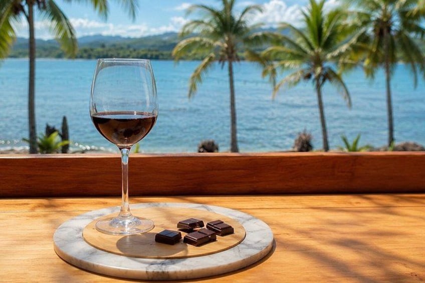 A glass of red wine on a wooden table with a marble coaster, surrounded by chocolate pieces, with a tropical beach and palm trees in the background. 1