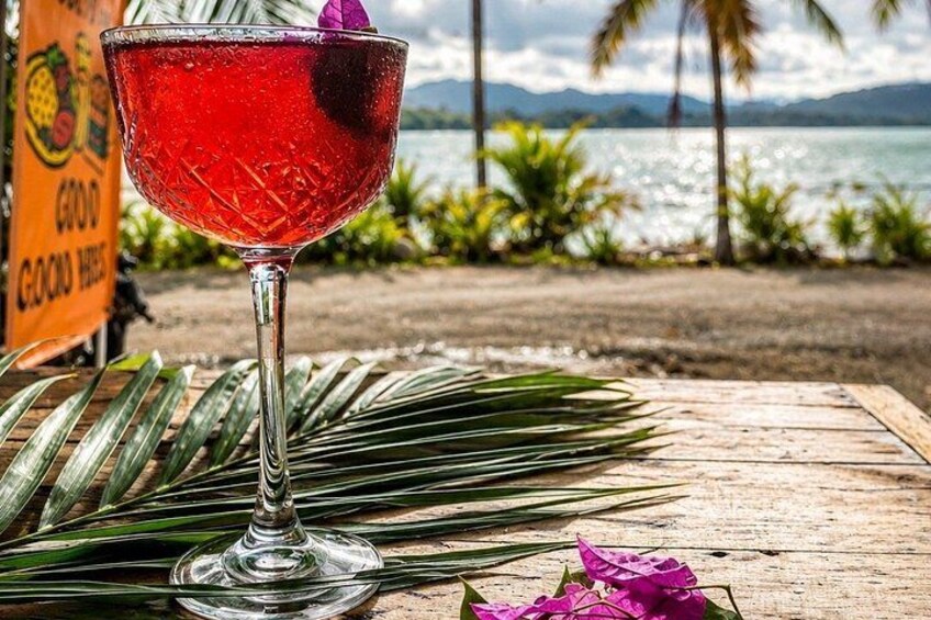 A cocktail glass on a wooden table with a tropical beach and palm trees in the background. 5