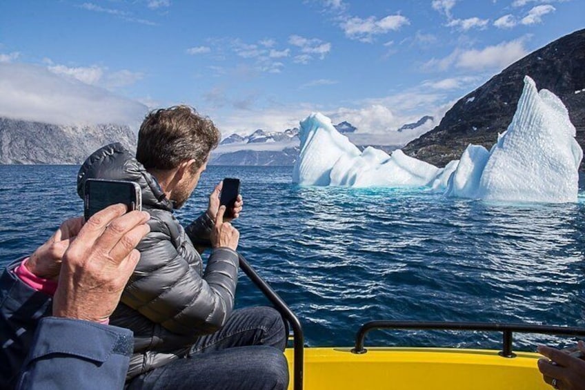 A person taking a photo of an iceberg with a boat. 2